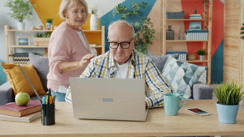 Un couple de personnes âgées, le mari devant son pc portable