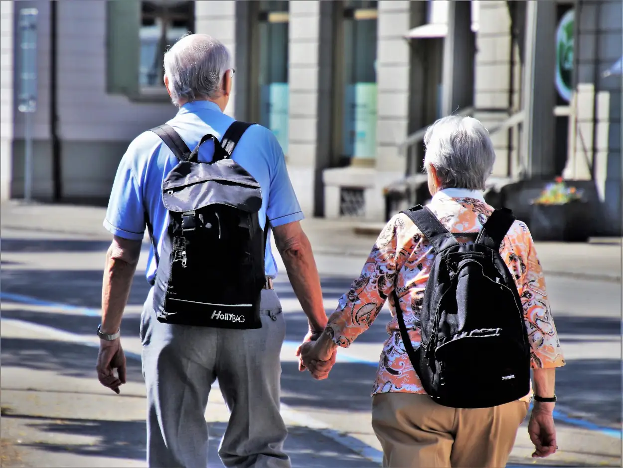 couple de personnes âgées qui se promènent en rue avec un sac sur le dos. Ils se tiennent main dans la main