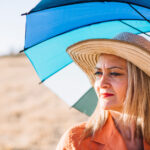 Une femme sous le soleil , elle porte un chapeau et se protège avec une ombrelle