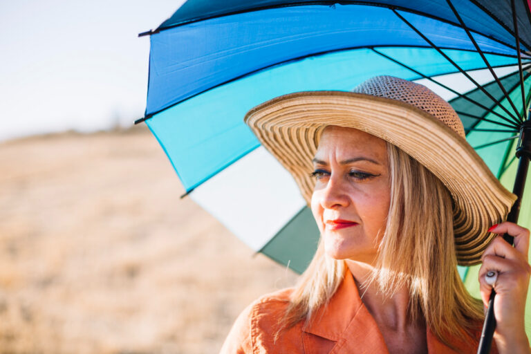 Une femme sous le soleil , elle porte un chapeau et se protège avec une ombrelle